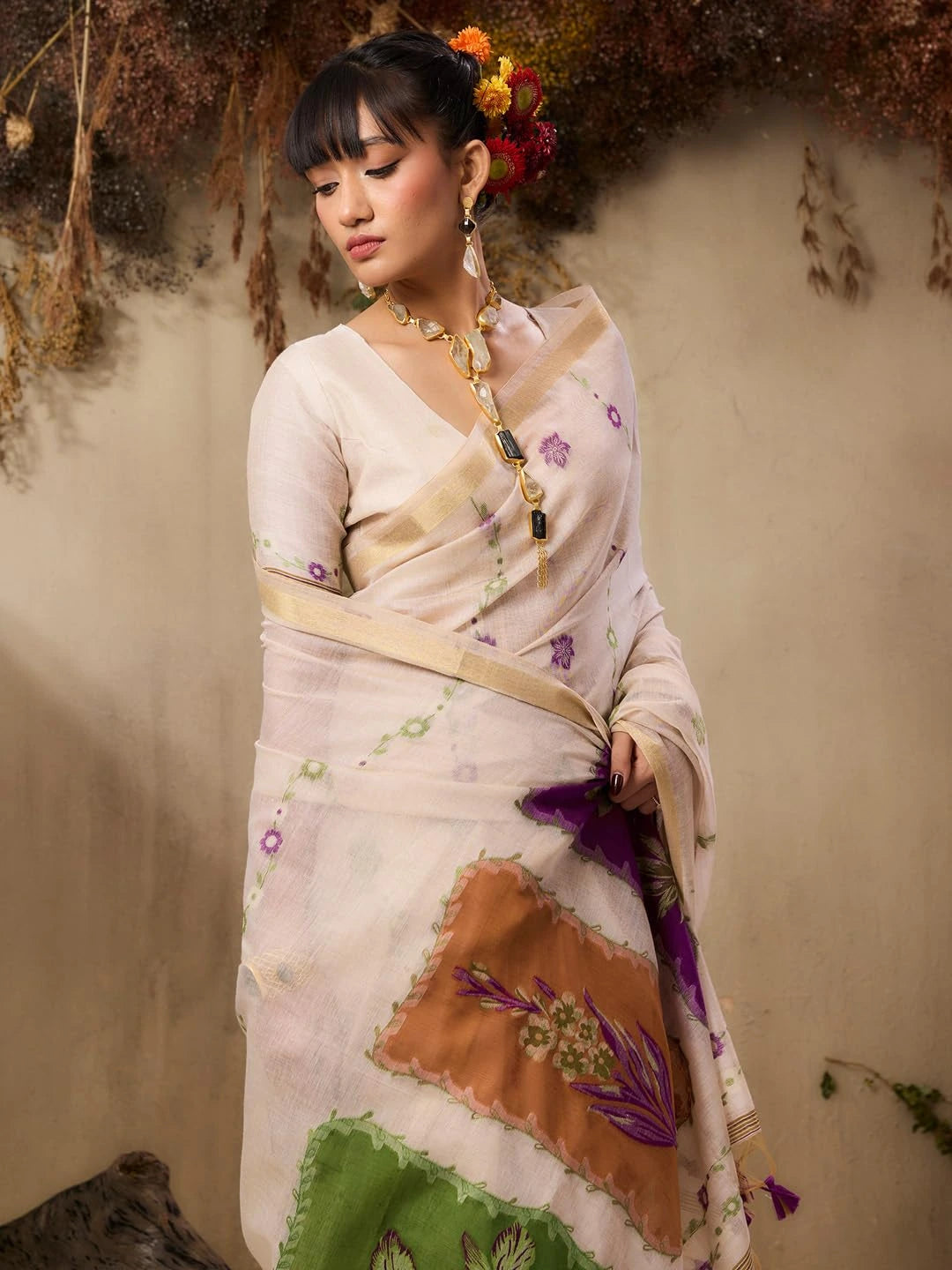 A woman stands elegantly in a soft pastel pink saree with delicate floral embroidery and printed motifs.